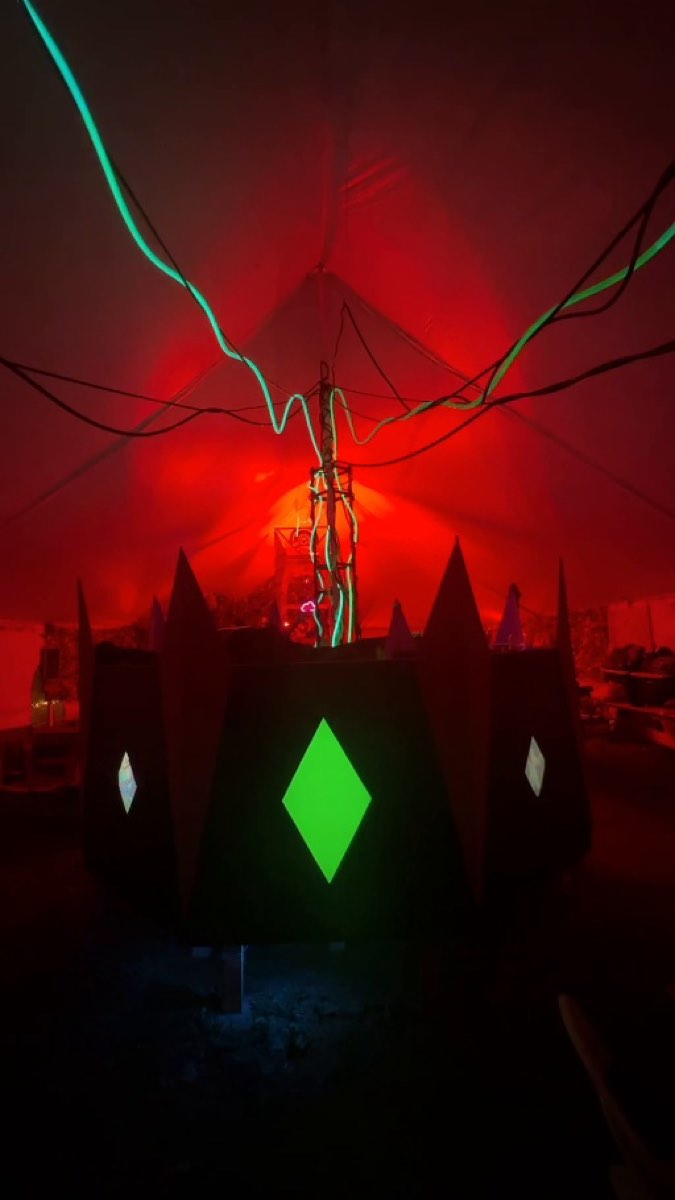 The Antropique DJ booth under red light, with six illuminated tubes rising from behind it into the tent