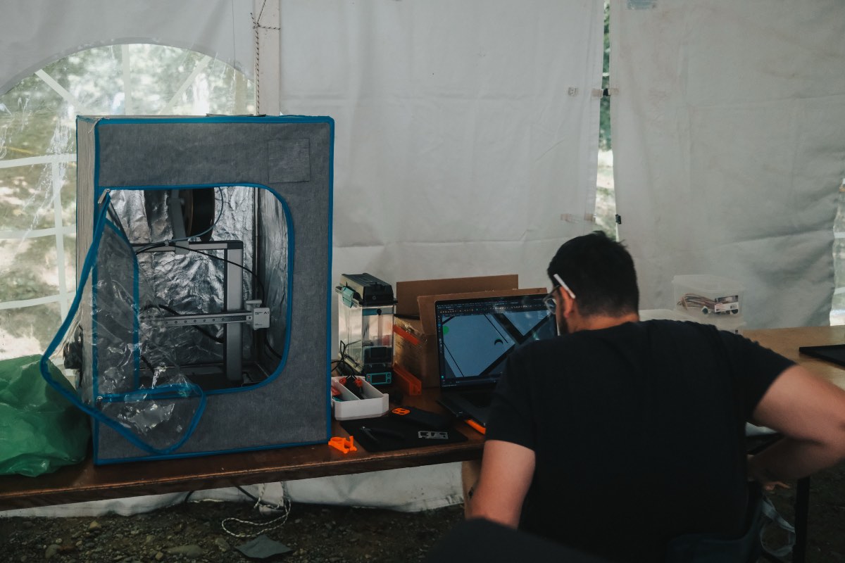 3D modelling beside the enclosed 3D printer in the tent